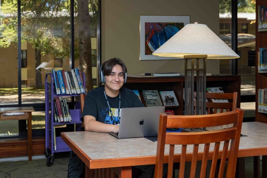 A student smiles at the camera while working on their computer at the Bonisteel library at Interlochen Arts Academy.