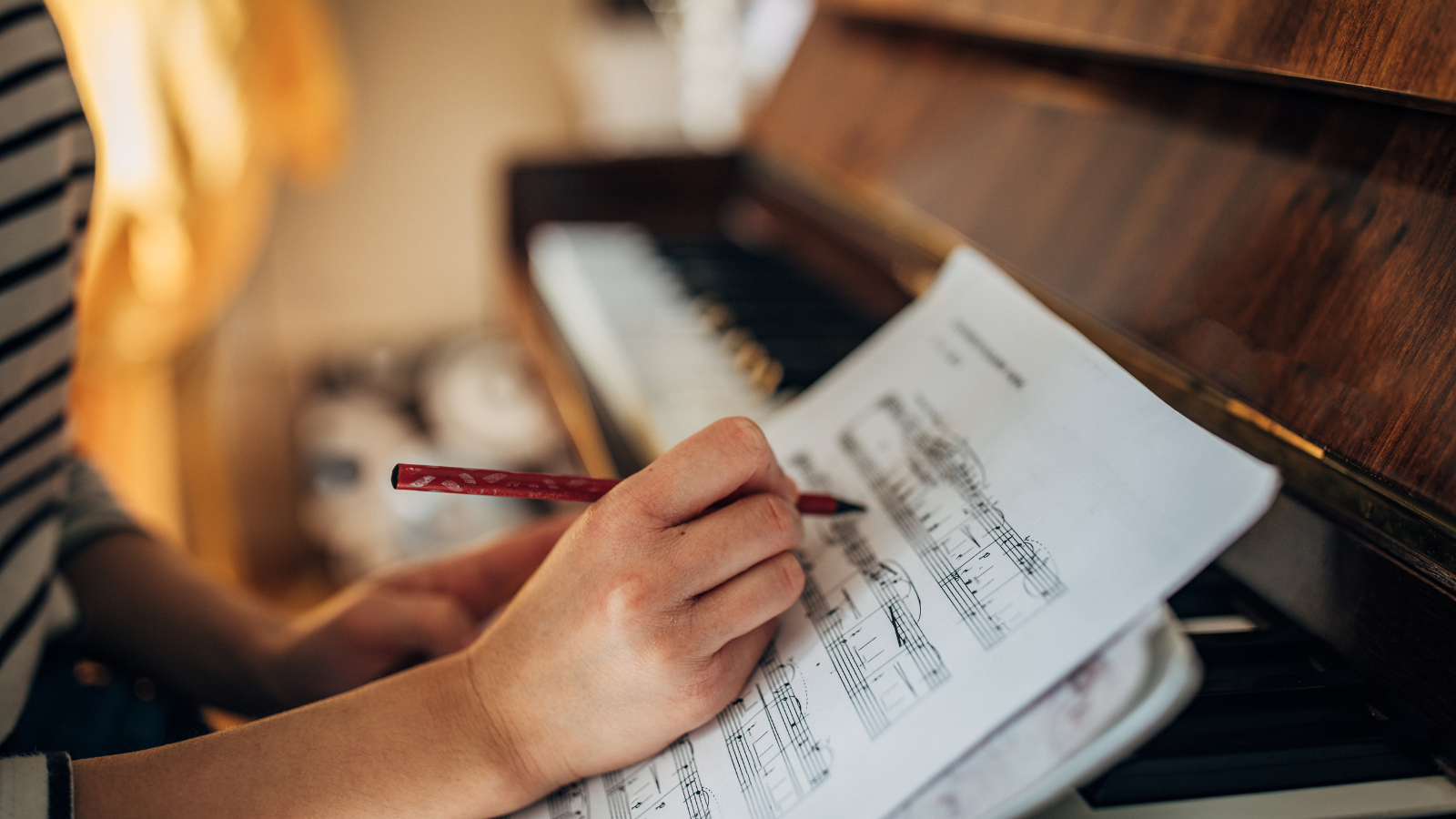 A woman writing on sheet music by a piano.