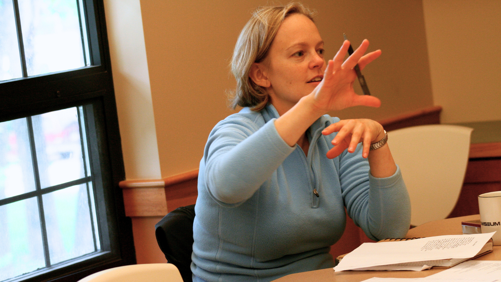 A woman talking with papers in front of her.