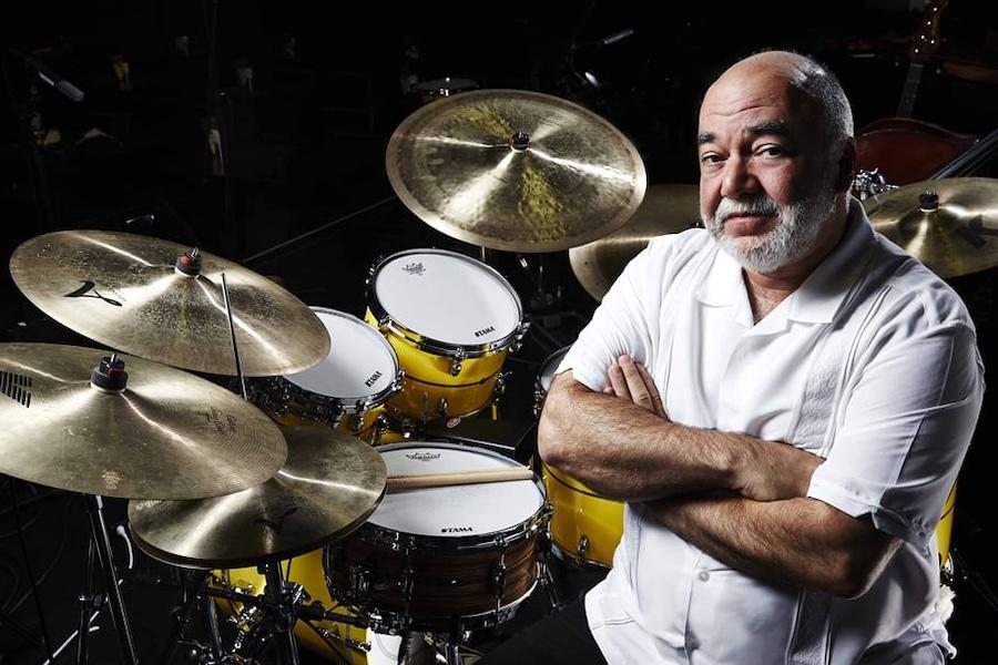Peter Erskine sitting with arms crossed behind a professional drum set.