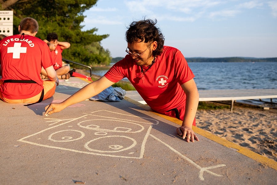 An Arts Camp lifeguard sketches a cartoon character on the sidewalk outside the Boat Cave. 