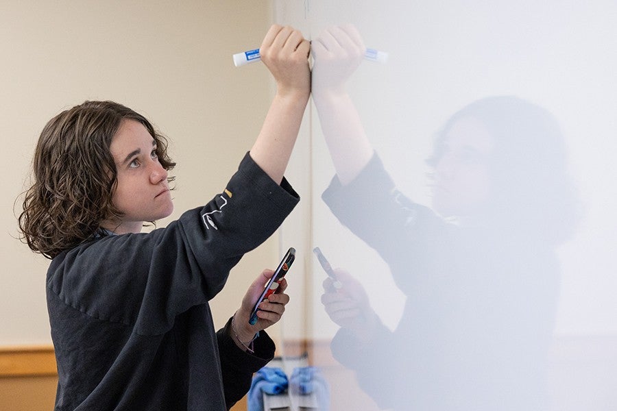 A high school creative writing student writes on a whiteboard during a playwriting workshop. 