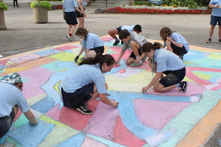 Visual arts students create a chalk drawing of the Comedy of Errors artwork during the pre-Collage festivities on Osterlin Mall.