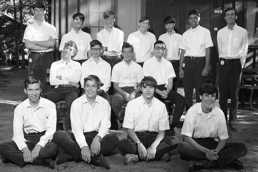 A group of eleven young men and their counselors pose for a photo outside cabin HSB10 