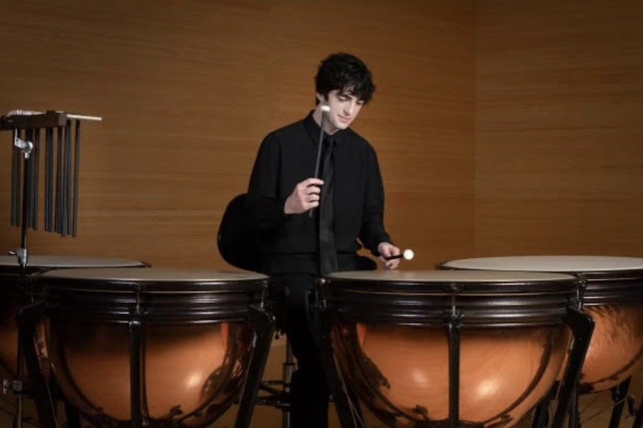 Dressed in a dark suit, a student performs on the drums