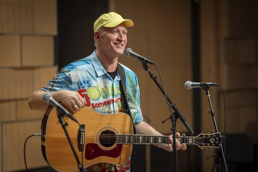 An alumnus in a colorful shirt poses with his guitar.