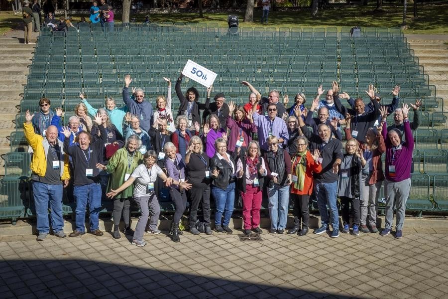 A large group of alumni pose with a sign reading "50th".