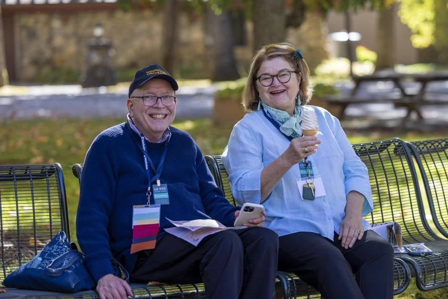 Two alumni smile while sitting on benches; one holds an ice cream cone.