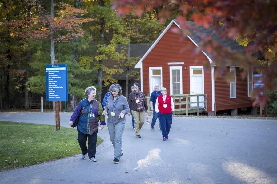 A group of alumni stroll campus under fall leaves.