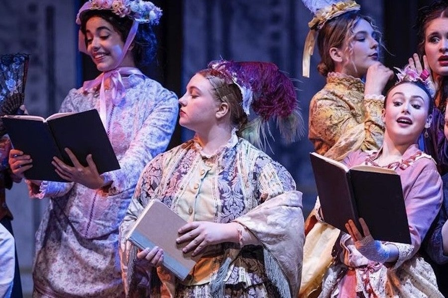 A group of students sing in Victorian-era costumes.