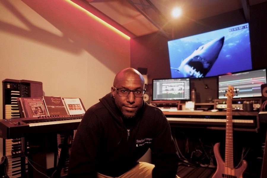 Levi Taylor poses in his composition studio with a large picture of a shark visible on the computer screen behind him.