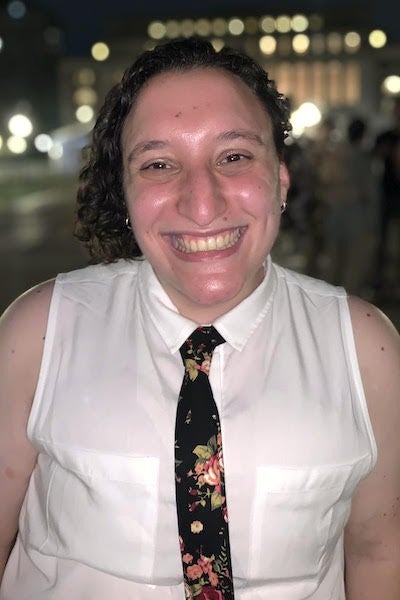 Jenna Zucker smiles at the camera in a night photograph with city lights in the background. 