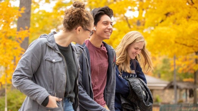 Three students walk across a fall campus