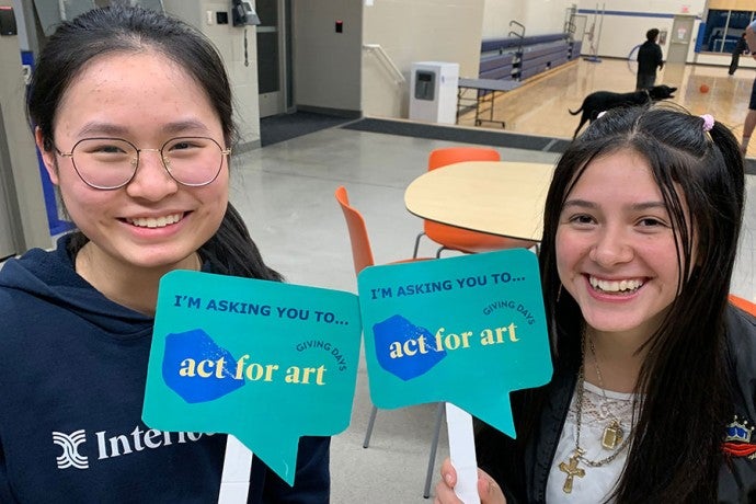 Two students hold signs reading 'I'm asking you to Act for Art'