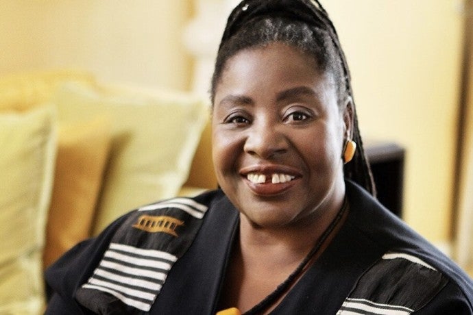 A dark-skinned woman wearing a white and black shirt smiles at the viewer.