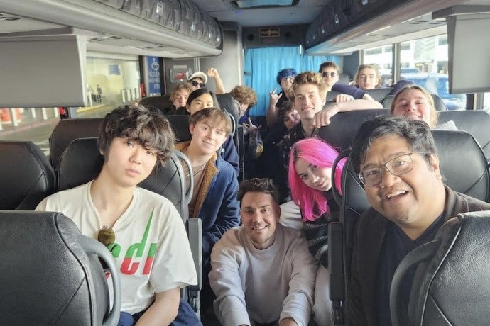 A group of students and instructors smile while riding a bus.