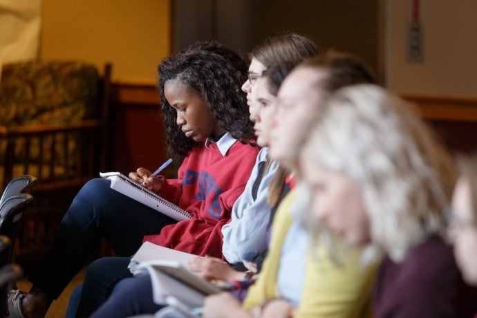 A row of girls writing in their notebooks with a focus on the girl at the end in deep concentration on what she is writing