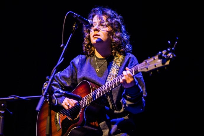 A spotlight on a person singing into a mic while playing the guitar