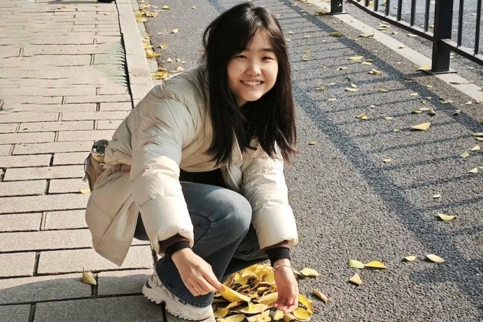 A girl smiles as she bends to pick up some fall leaves.