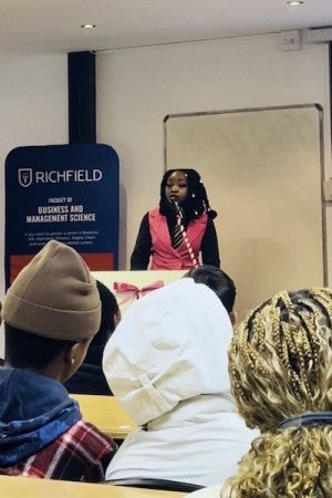 Mwila Keso stands at a Richfield College podium in front of an audience.