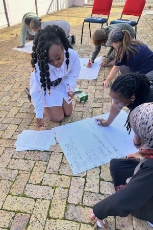 Mwila Keso kneels on the ground with survivors, teaching a class in human rights.