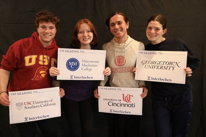 A group of students wearing sweatshirts and carrying signs representing various colleges and university poses for the camera.