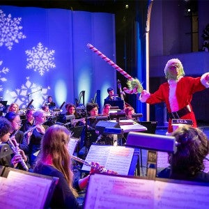 The grinch conducts an orchestra while waving a giant candy cane