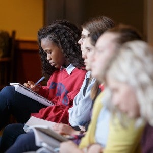 A row of girls writing in their notebooks with a focus on the girl at the end in deep concentration on what she is writing