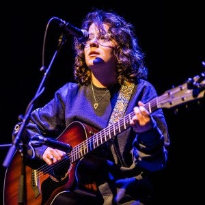 A spotlight on a person singing into a mic while playing the guitar