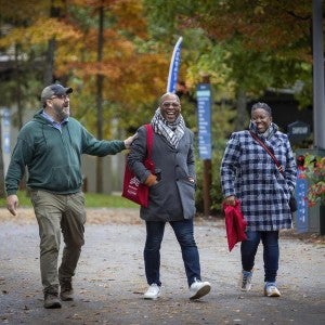 Three smiling alumni explore campus during the fall.