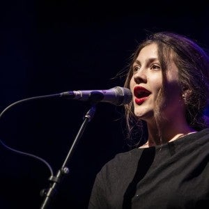 A student wearing a black dress sings into a microphone.