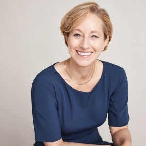 Professional headshot of a blonde woman wearing a navy blue top.