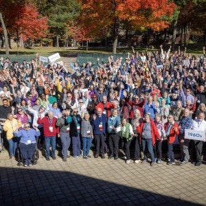 A large group of excited alumni smile and wave their hands.