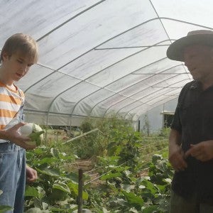 A film student talks with a farmer in a hoop house.