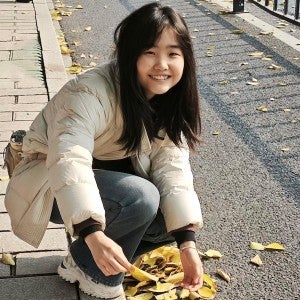 A girl smiles as she bends to pick up some fall leaves.