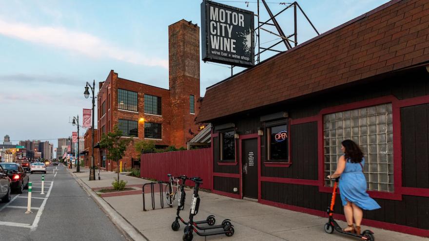 Street view showing the "Motor City Wine" bar and shop with a woman riding a scooter in front.