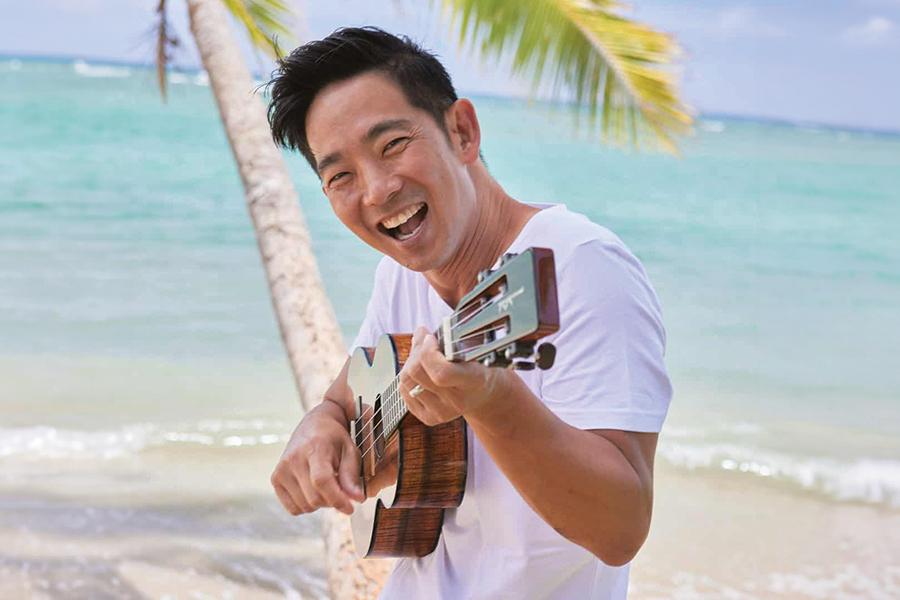 A man smiles on the beach with a ukulele